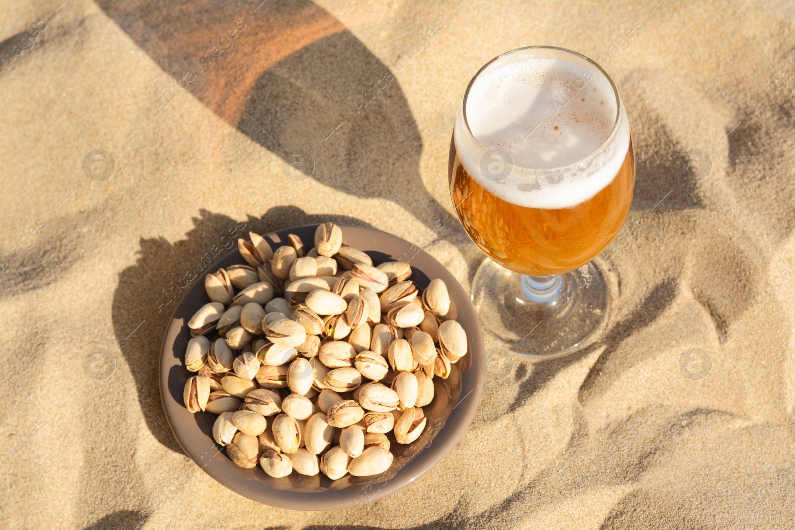 Photo of Glass of cold beer and pistachios on sandy beach, above view