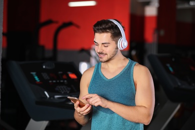 Young man with headphones listening to music on mobile device at gym