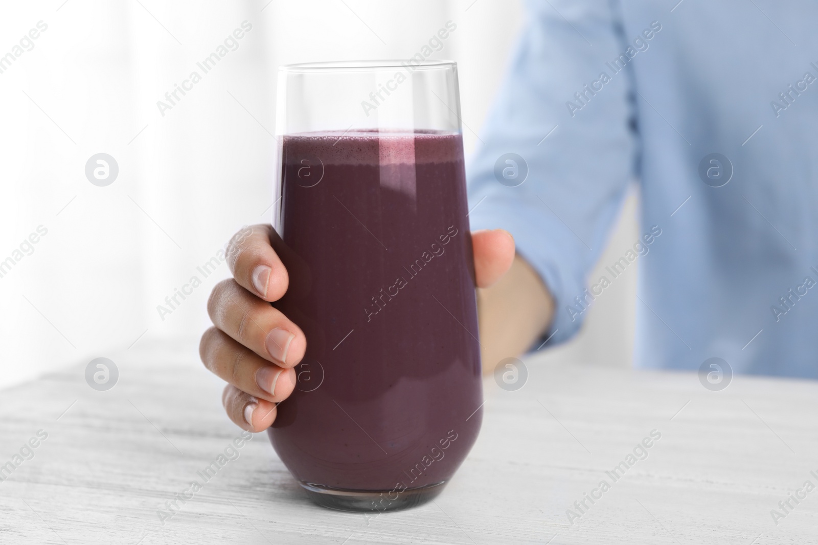 Photo of Woman with glass of fresh acai drink at white wooden table, closeup