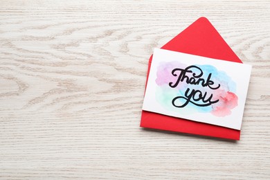 Photo of Envelope and card with phrase Thank You on light wooden table, top view. Space for text