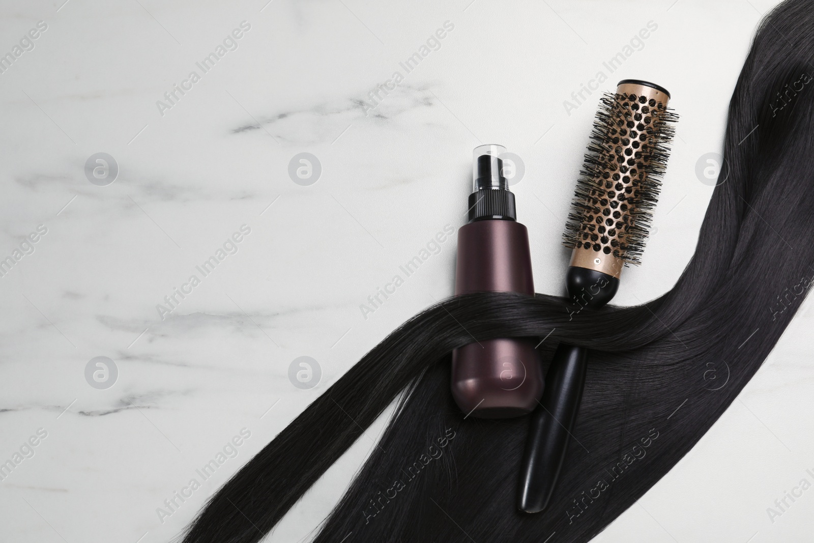 Photo of Spray bottle with thermal protection, lock of brunette hair and hairbrush on white marble table, flat lay. Space for text