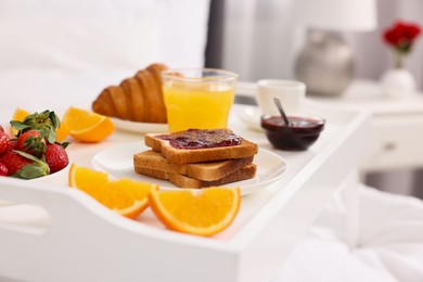 Photo of Tray with delicious breakfast on bed in room, closeup