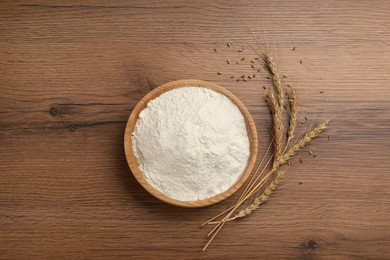 Photo of Bowl of flour and wheat ears on wooden table, flat lay