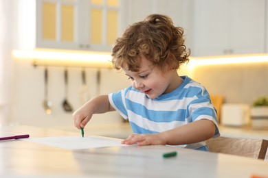 Photo of Cute little boy drawing with marker at table in kitchen