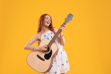 Photo of Beautiful young hippie woman playing guitar on orange background