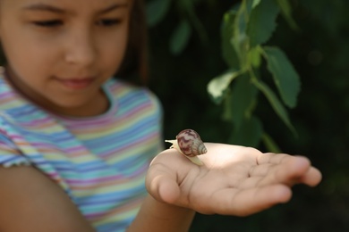 Girl playing with cute snail outdoors, focus on hand. Child spending time in nature