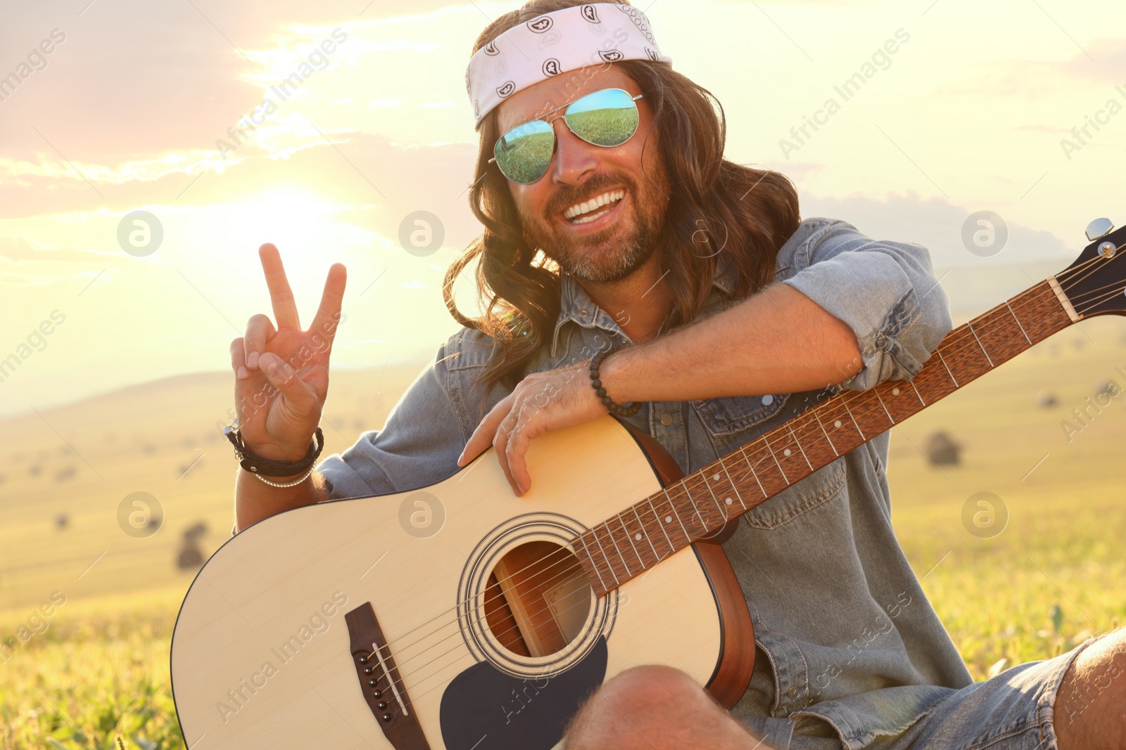 Photo of Happy hippie man with guitar showing peace sign in field