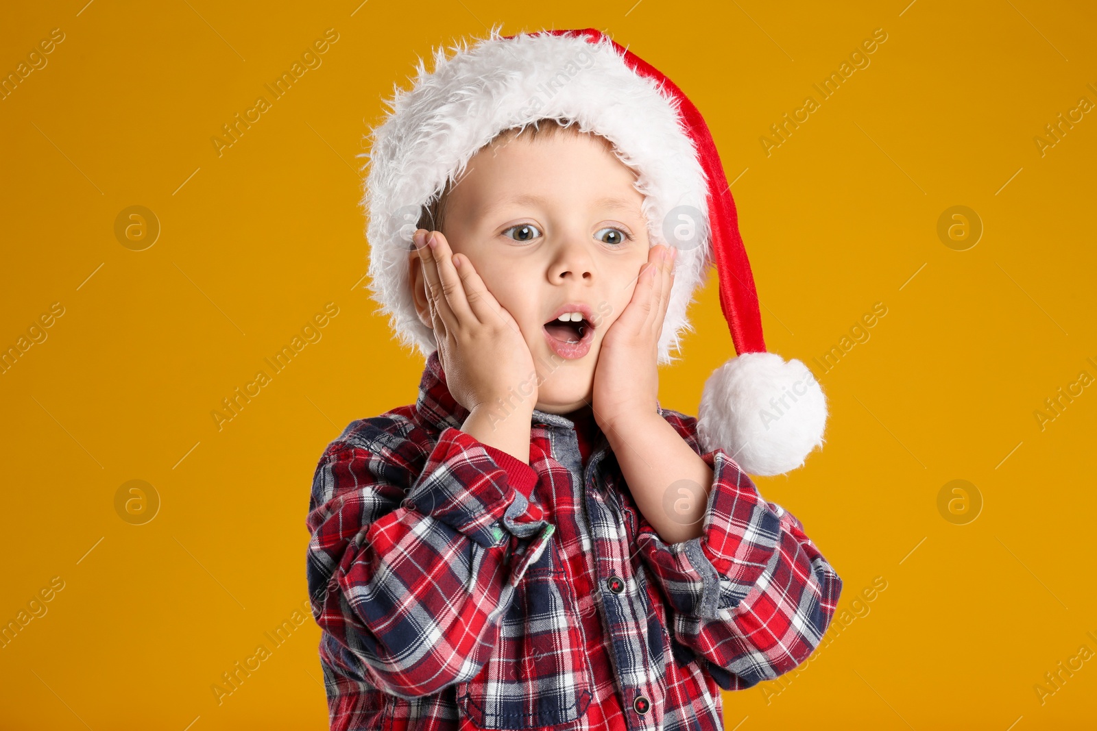 Photo of Cute child in Santa hat on yellow background. Christmas celebration