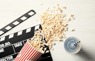 Photo of Tasty popcorn, drink and clapperboard on wooden background, top view. Cinema snack