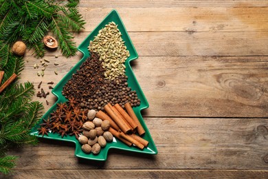 Different spices, nuts and fir branches on wooden table, flat lay. Space for text