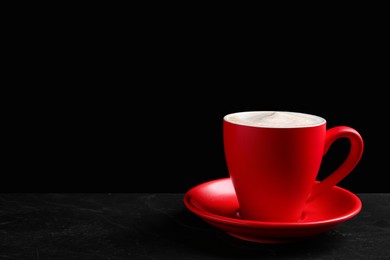 Photo of Red cup with aromatic cappuccino on black textured table. Space for text