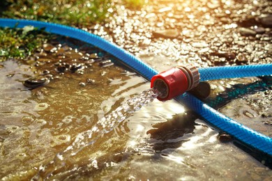 Water flowing from hose on ground outdoors, closeup. Space for text