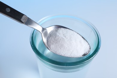 Photo of Spoon with baking soda over glass of water on light blue background, closeup