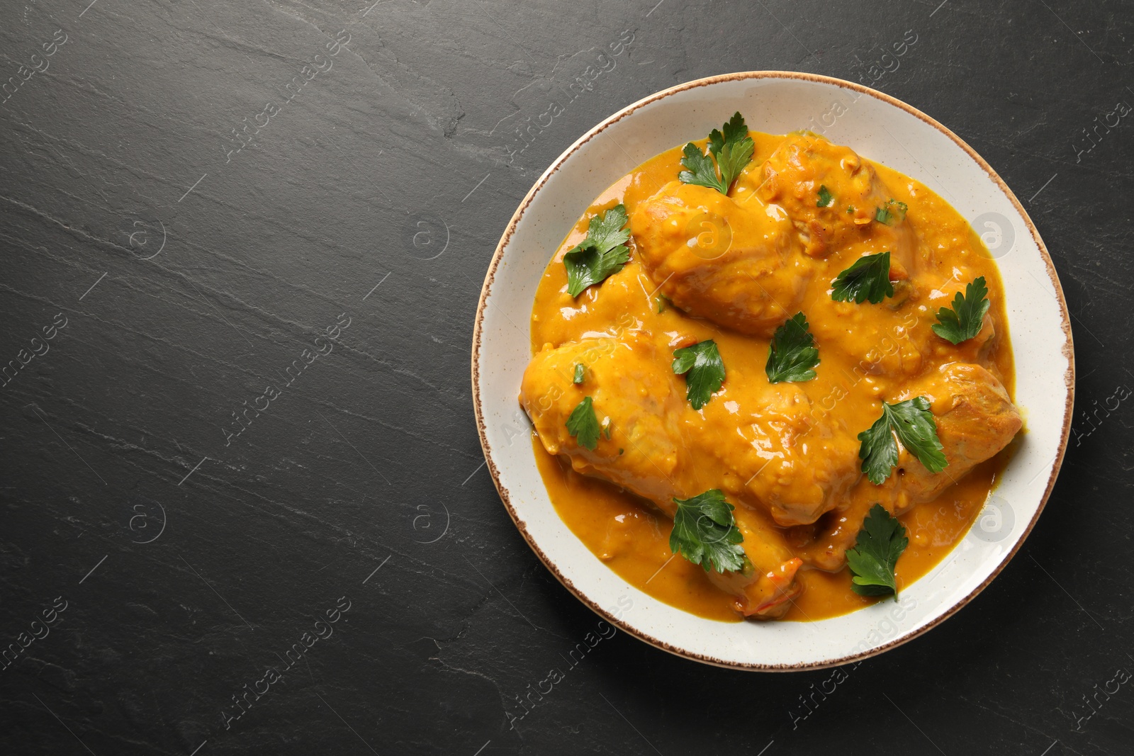 Photo of Tasty chicken curry with parsley on black textured table, top view. Space for text
