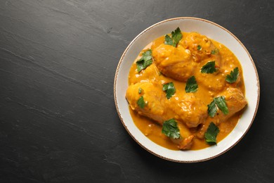 Tasty chicken curry with parsley on black textured table, top view. Space for text