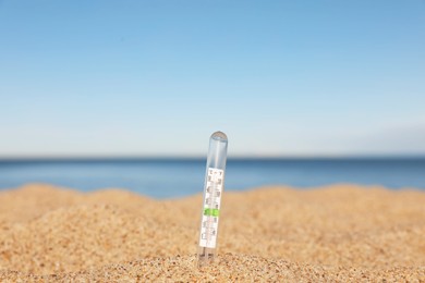 Weather thermometer in sand near sea, space for text