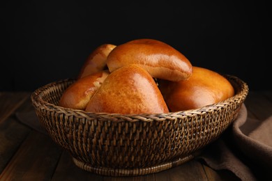 Wicker basket with delicious baked pirozhki on wooden table