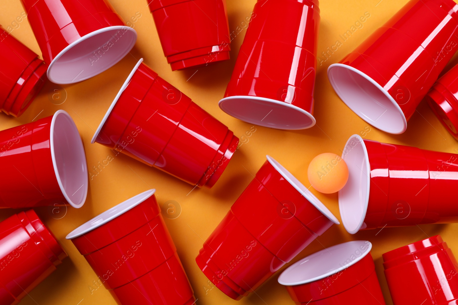 Photo of Plastic cups and ball for beer pong on orange background, flat lay