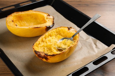 Photo of Baking sheet with halves of cooked spaghetti squash and spoon on wooden table, closeup
