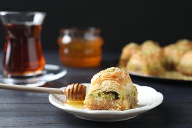 Photo of Delicious fresh baklava and honey with chopped nuts on black wooden table, closeup. Eastern sweets