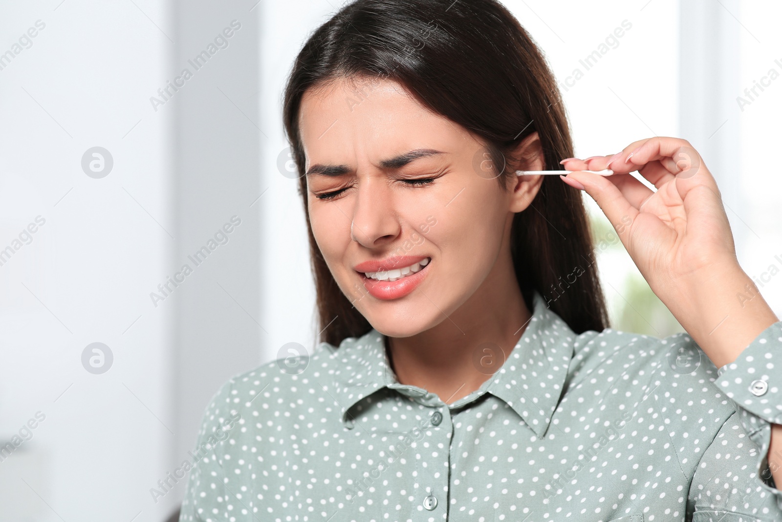 Photo of Young woman cleaning ear with cotton swab indoors