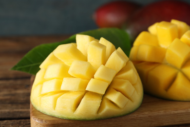 Photo of Halves of ripe mango cut into cubes on wooden table