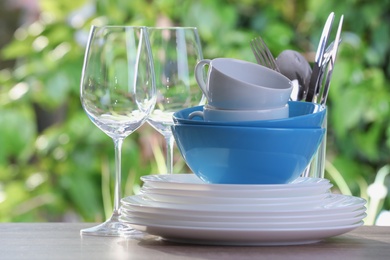 Photo of Clean dishes, cups, shiny cutlery and glasses on wooden table against blurred background