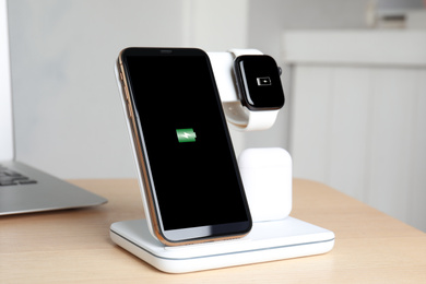 Photo of Set of gadgets charging with wireless pad on wooden table indoors