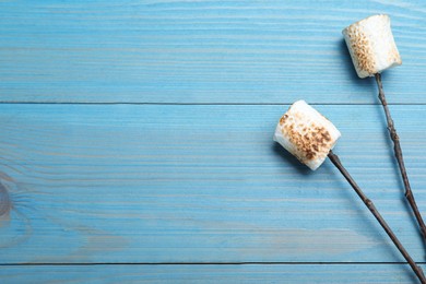 Sticks with roasted marshmallows on light blue wooden table, flat lay. Space for text