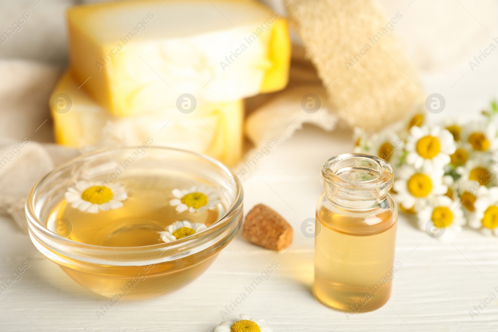 Photo of Essential oil and chamomiles on white wooden table