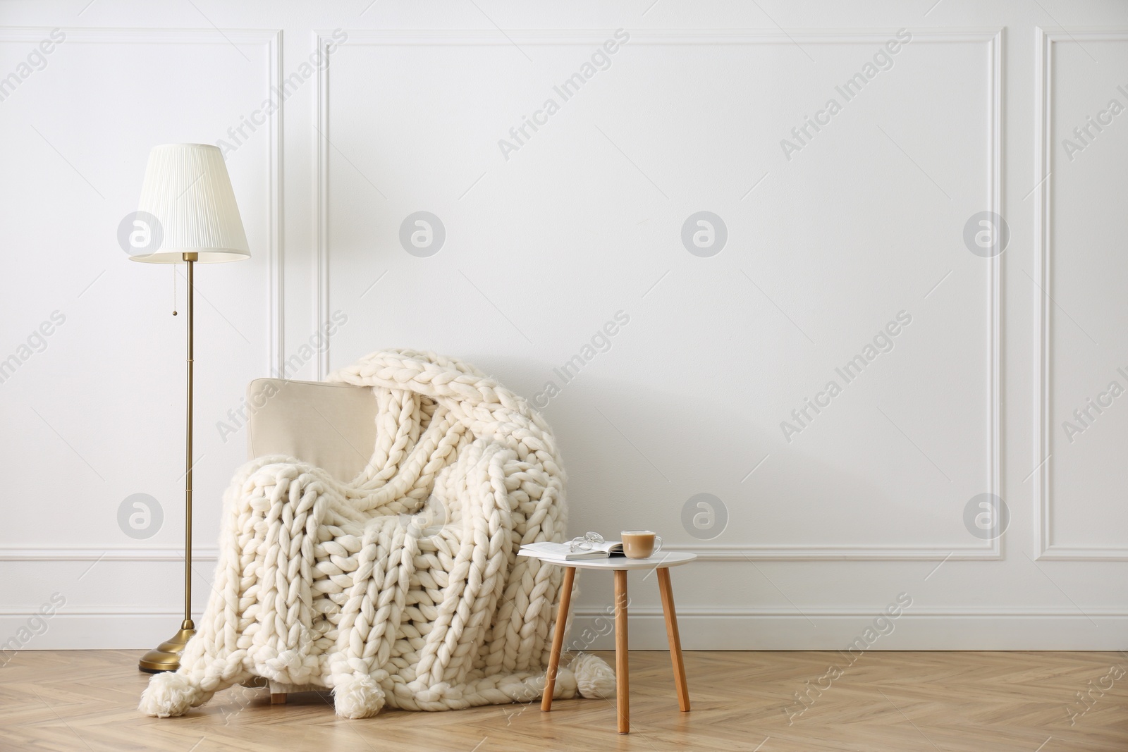 Photo of Knitted merino wool plaid on armchair in room. Space for text