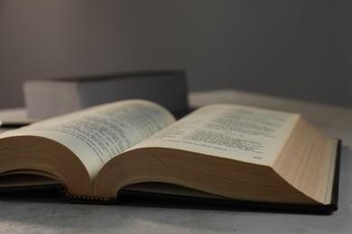 Closeup view of open hardcover Bible on grey table indoors. Religious book