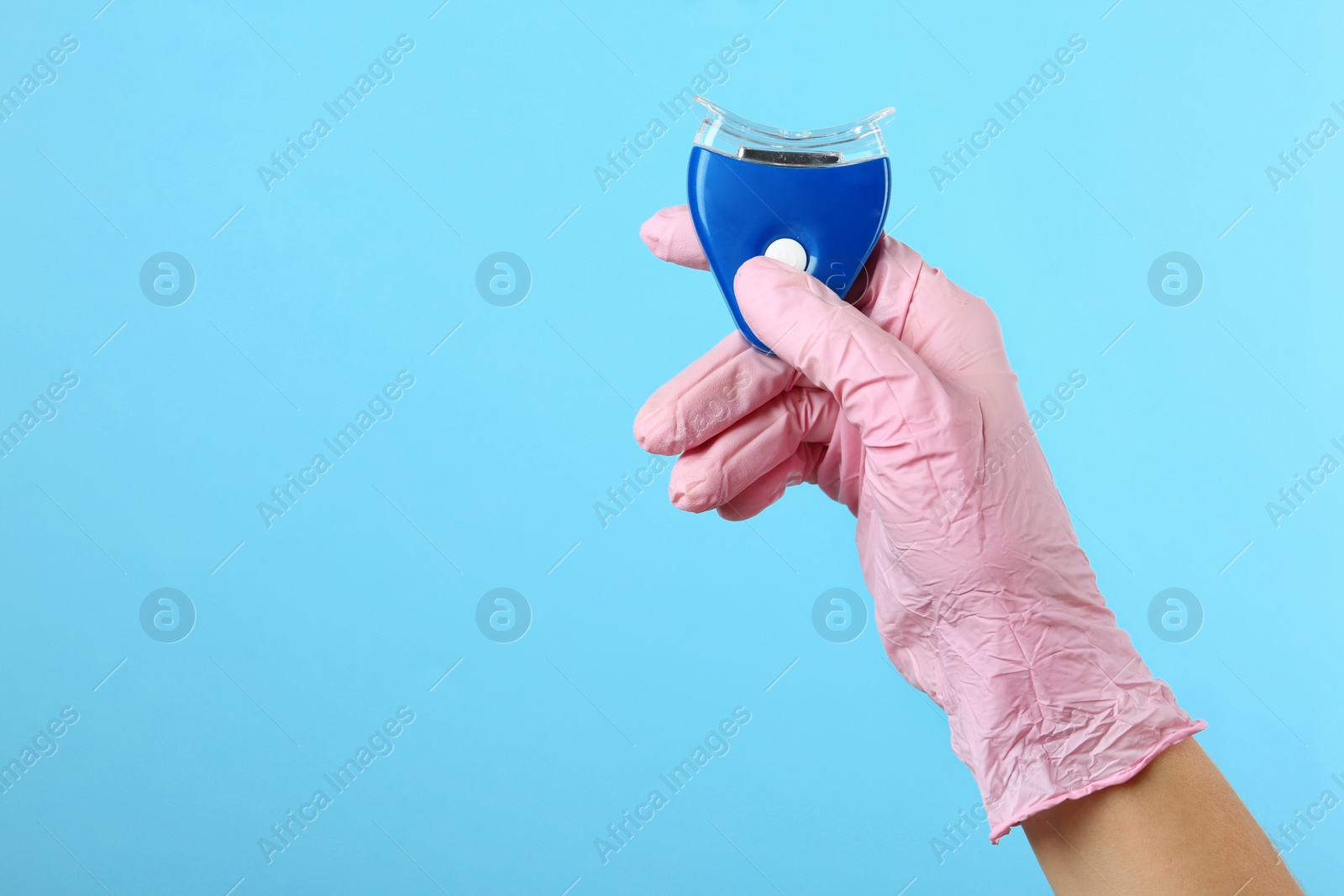 Photo of Dentist holding teeth whitening device on color background, space for text