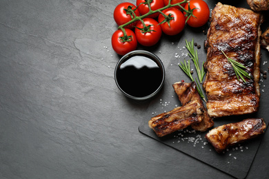 Photo of Delicious grilled ribs on black table, flat lay. Space for text