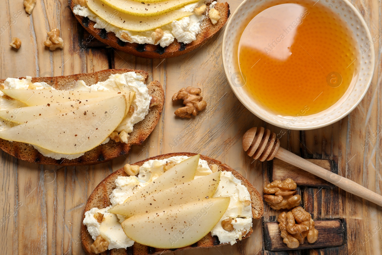 Photo of Toasted bread with tasty cream cheese and pear on wooden table, flat lay