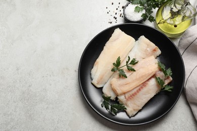 Plate with raw cod fish, parsley, oil and spices on light textured table, flat lay. Space for text