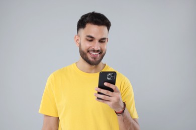 Happy young man using smartphone on grey background