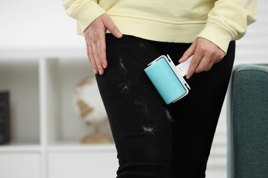 Photo of Woman with lint roller removing pet hair from black trousers indoors, closeup. Space for text