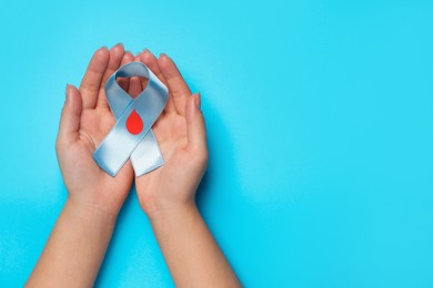 Photo of Woman holding light blue ribbon with paper blood drop on color background, top view and space for text. Diabetes awareness