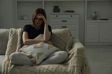 Photo of Sad young woman sitting on sofa at home, space for text