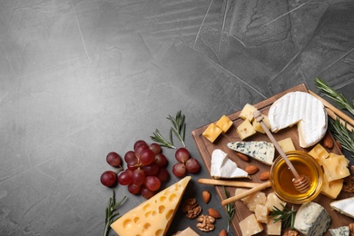 Cheese plate with honey, grapes and nuts on grey table, flat lay, Space for text