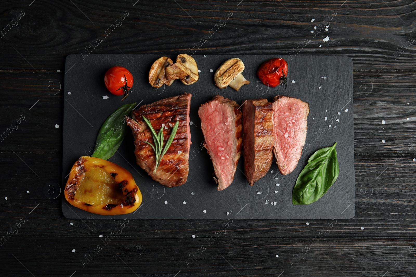 Photo of Board with slices of grilled meat on black wooden table, top view
