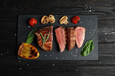 Photo of Board with slices of grilled meat on black wooden table, top view
