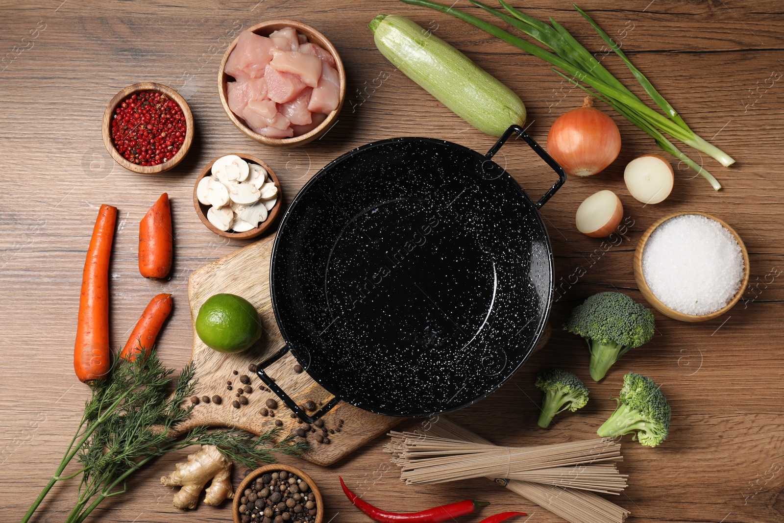 Photo of Empty iron wok surrounded by raw ingredients on wooden table, flat lay