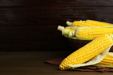 Tasty fresh corn cobs on wooden table, space for text