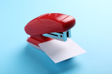 Photo of One new bright stapler with paper note on light blue background, closeup