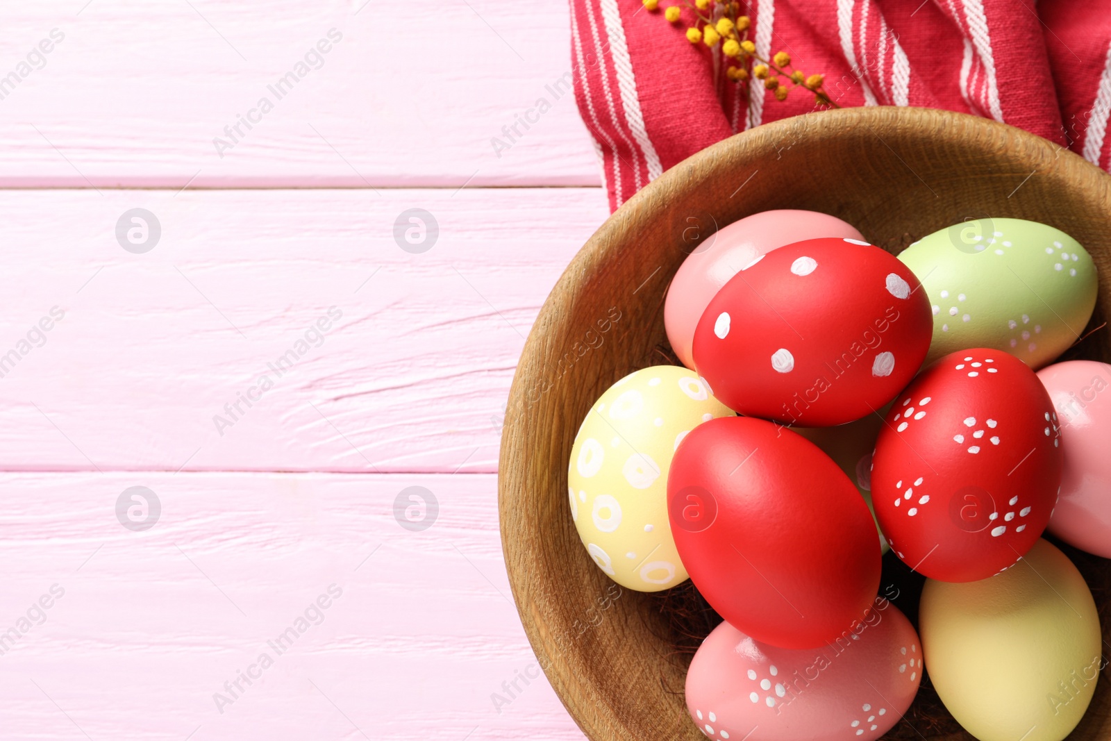 Photo of Bowl with painted Easter eggs and napkin on wooden table, flat lay. Space for text