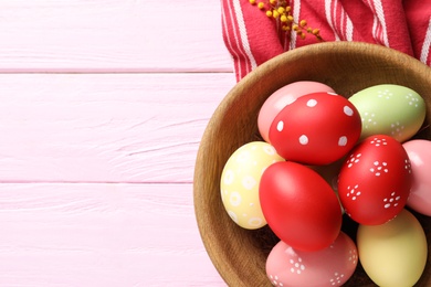 Photo of Bowl with painted Easter eggs and napkin on wooden table, flat lay. Space for text