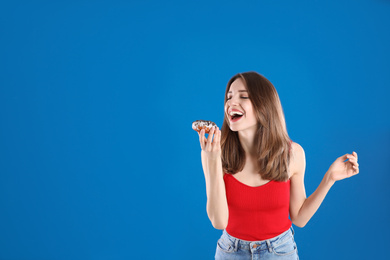 Photo of Beautiful young woman with donut on blue background. Space for text