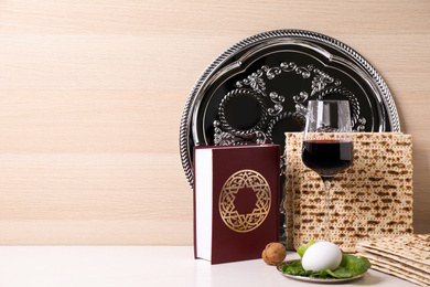 Photo of Symbolic Pesach (Passover Seder) items on white table against wooden background, space for text